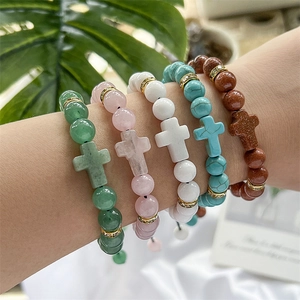 Detailed view of five natural stone bracelets with cross pendants on a wrist