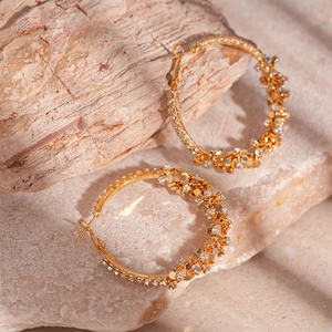 Macro detail of gold geometric hoop earrings with sparkling white zircons on a stone