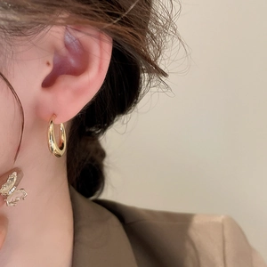 Close-up of a model wearing a polished gold C-shaped hoop earring with a metallic finish