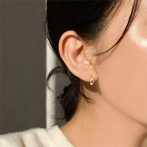 Close-up of minimalist silver oval huggie hoop earring worn by a model in warm light