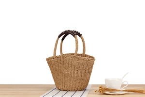 Detail of woven straw handbag with brown leather handles and white stitching details