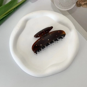 Detailed top view of an amber hair claw clip with colorful rhinestones on a white tray