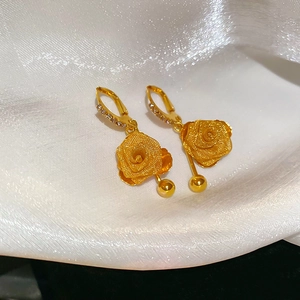 Detail of gold rose earrings with crystal accents and polished beads on white silk