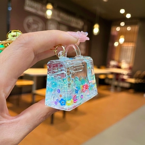 Handheld view of a mini transparent handbag keychain with colorful floral glitter filling