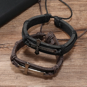 Close-up of black and brown braided leather bracelets with engraved cross in Spanish
