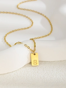 Vue macro du pendentif carré en acier inoxydable doré avec la lettre S gravée dessus