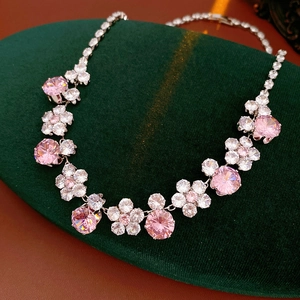 Macro view of pink and white crystal flower link necklace on dark green velvet padding