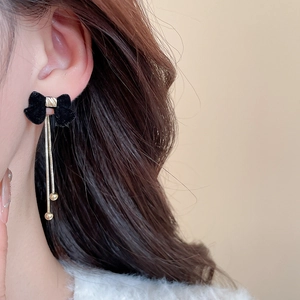 Close-up of black velvet bow earrings with long golden metal chain tassels on model