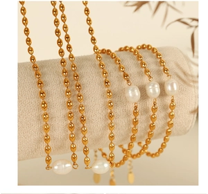 Close-up of gold beaded chain with freshwater pearls displayed on a beige stand
