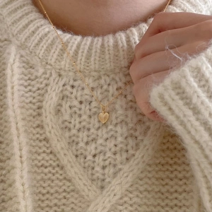 Detailed view of a golden heart necklace with ribbed texture on a white knit sweater