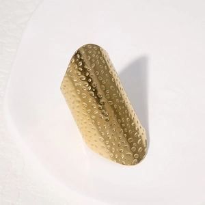 Detail shot of golden wide band ring with hammered texture on white ceramic tray