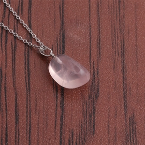 Close-up of a pink quartz stone pendant with a delicate silver chain on wood surface
