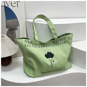 Detail of green canvas tote bag featuring black floral art print and NKK studio design