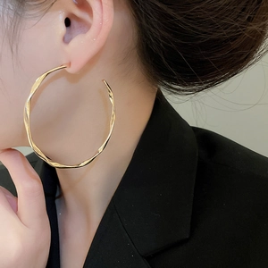 Close-up of model wearing large gold twisted hoop earrings with a metallic texture