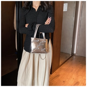 Silver square handbag featuring bow accents and metallic chain strap shown in a home setting