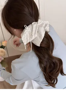 Close-up of a white polka dot bow scrunchie with long ribbons on a model's hair