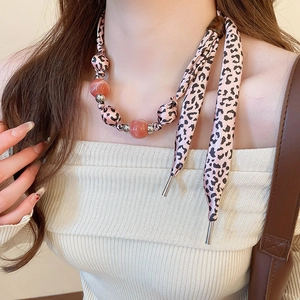 Détail d'un collier nœud en soie à imprimé léopard rose avec perles sur mannequin