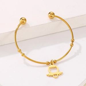 Detailed close-up of golden titanium steel cuff with heart wing pendant on stone background