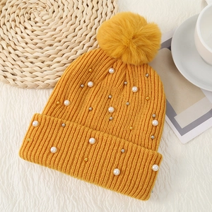 Detail of yellow knit beanie featuring fluffy pompom, pearls, and metallic beads decoration