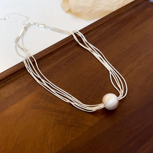 Collana multistrato argentata minimalista con pendente di perla su fondo in legno