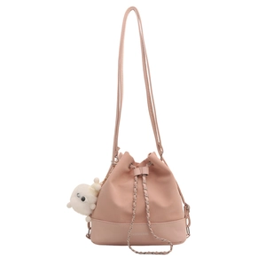 Pink bucket style crossbody bag with chain strap and cute plush charm on white background