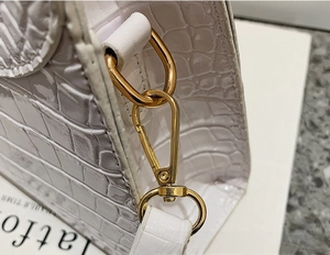 Detail of white crocodile-embossed leather handbag with shiny gold lobster clasp hardware