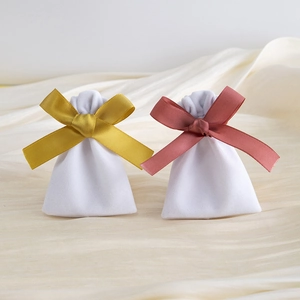 Detail of soft white velvet jewelry pouches with decorative yellow and pink ribbon bows
