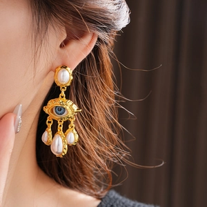 Close-up of vintage baroque style gold earrings with white pearls and blue eye motif