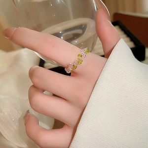 Close-up of pink and green beaded flower ring worn on hand with aesthetic background