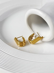 Detailed close-up of layered U-shaped golden wing earrings on a ceramic display