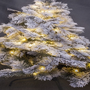 Dettaglio dell'albero di Natale floccato con rami innevati e luci LED calde