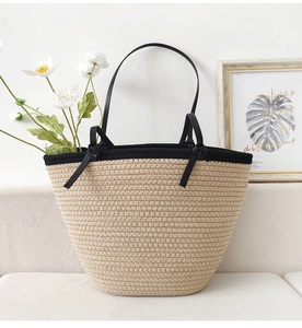 Detail of a woven beige raffia tote bag with black leather handles on a white sofa