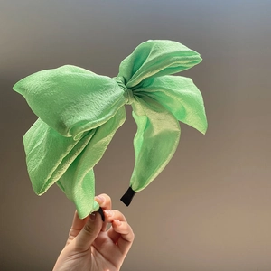 Close-up of green seersucker oversized bow headband held by hand in soft light