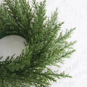 Gros plan d'une couronne d'aiguilles de pin artificielles vertes sur tissu blanc