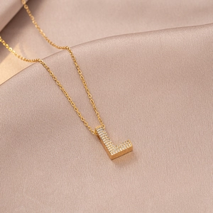 Detailed close-up of a gold necklace with a zircon-encrusted letter L pendant on silk