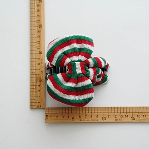 Detail of a festive red, white, and green striped knit bow hair clip on a white backdrop