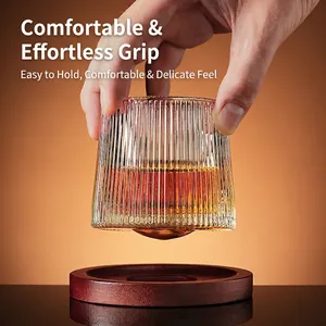 Vertical striped whiskey glass on wooden coaster being held with amber liquid