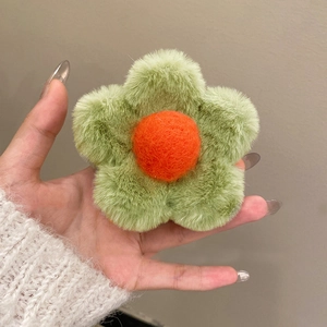 Detail view of plush flower hair claw featuring green petals and a soft orange center