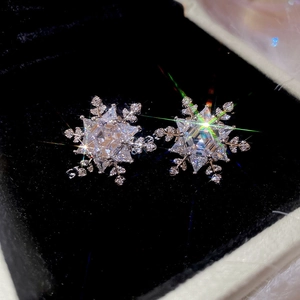 Macro shot of sparkling zircon snowflake stud earrings on a dark velvet jewelry box