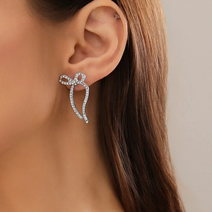 Detailed close-up of a silver bow earring with sparkling crystals on a female model