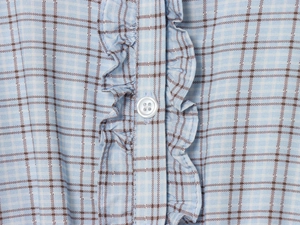 Detailed macro view of light blue plaid fabric with ruffled edges and a white button