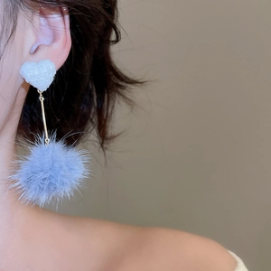 Dettaglio dell'orecchino a cuore con ciondolo a pompon blu su una modella