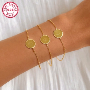 Detail of 925 sterling silver bracelets with gold finish and personalized letter pendants