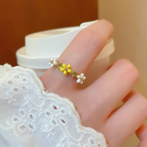 Close-up of golden flower ring with pearl and green gemstone worn on finger by a cup