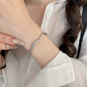 Detail of silver wavy metal bangle with polished finish on model wearing a white shirt