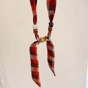 Close-up of red and black plaid fabric necklace with wood and ceramic bead accents