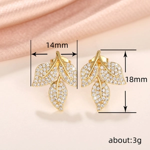 Elegant gold leaf earrings with white zircon pavé on a soft peach silk background
