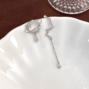Macro detail of asymmetric silver star and planet earrings with sparkling zircon stones