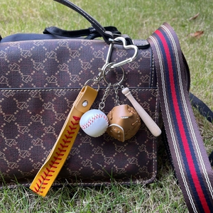 Mini baseball keychain with wooden bat and glove accessory hanging on a brown handbag