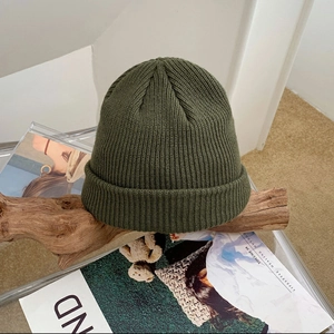 Close-up of army green ribbed knit beanie with vertical striped texture on a wooden stand